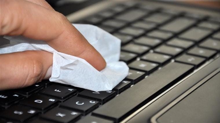 Hand wiping MacBook keyboard with cleaning cloth for a squeaky clean finish