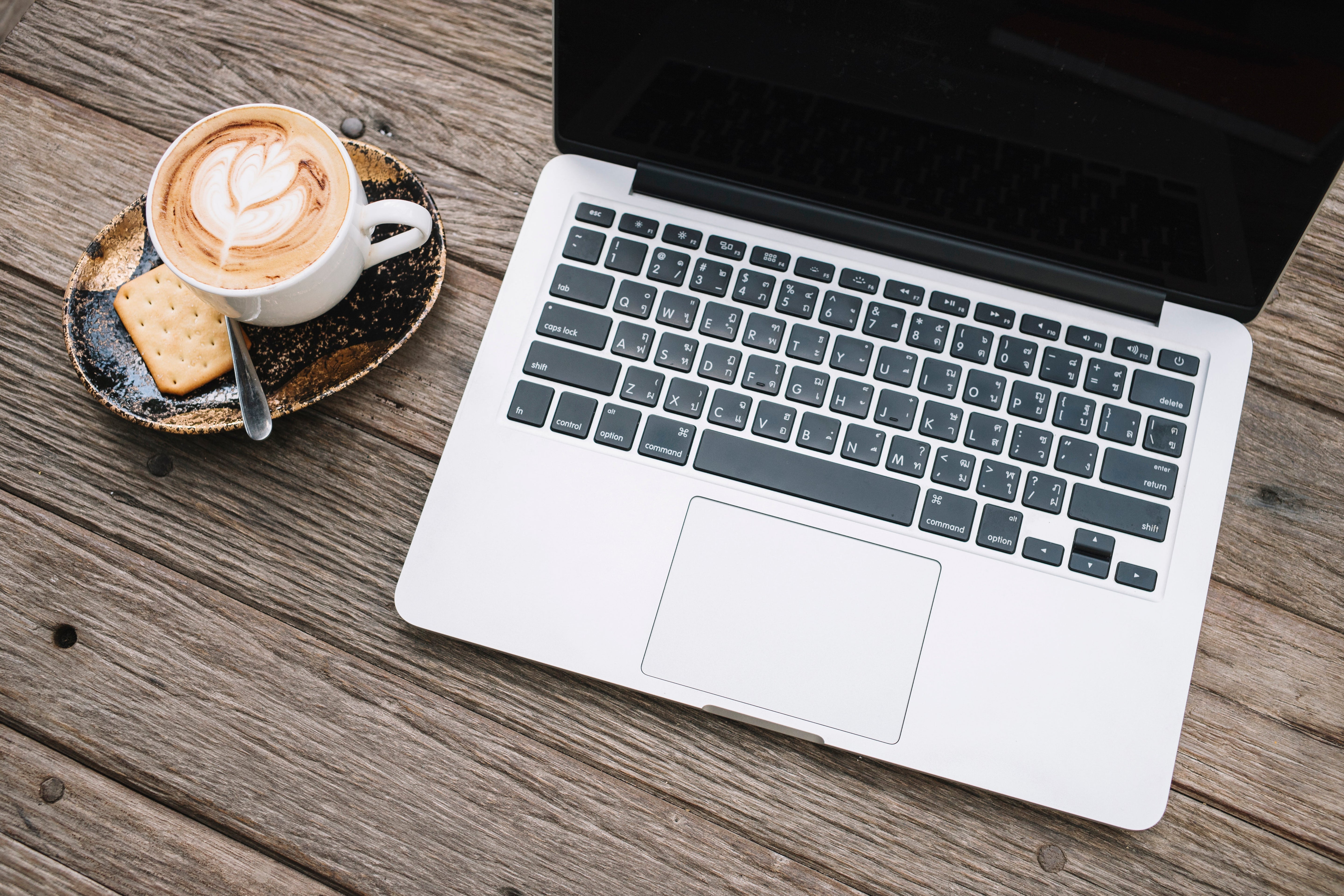 Sleek MacBook on wooden table beside latte and biscuit plate