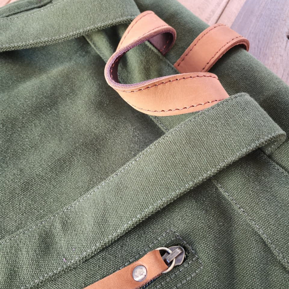 Detail of Zoodle Laptop Backpack's green canvas and tan leather zipper pull, highlighting durable stitching and quality materials.