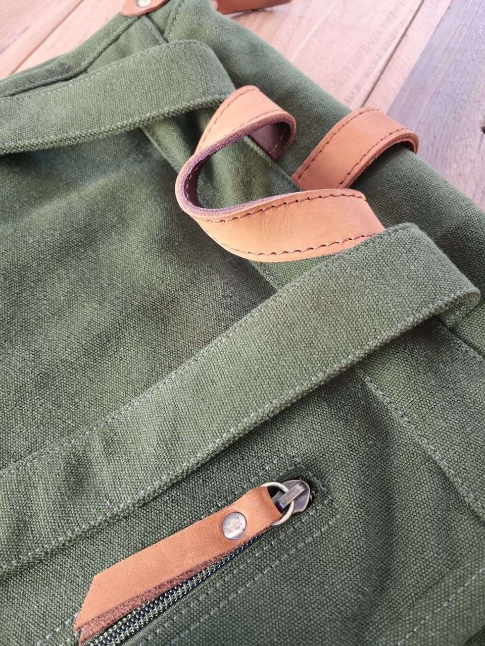 Detail of Zoodle Laptop Backpack's green canvas and tan leather zipper pull, highlighting durable stitching and quality materials.