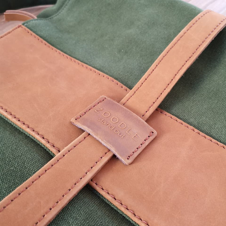 Close-up of Zoodle Laptop Backpack leather strap and embossed logo on tan leather flap, showcasing premium craftsmanship.