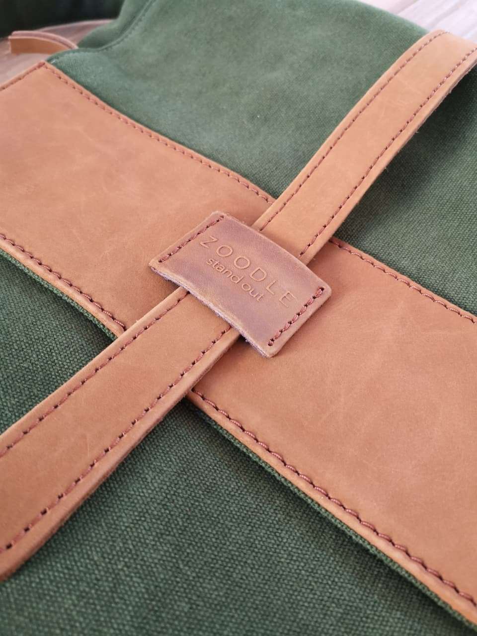 Close-up of Zoodle Laptop Backpack leather strap and embossed logo on tan leather flap, showcasing premium craftsmanship.