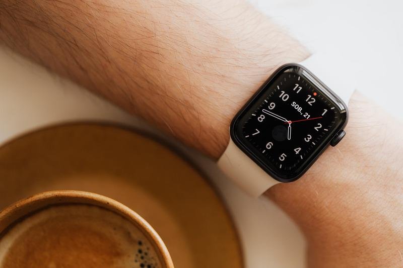 Stylish smart watch with white strap on wrist near coffee cup