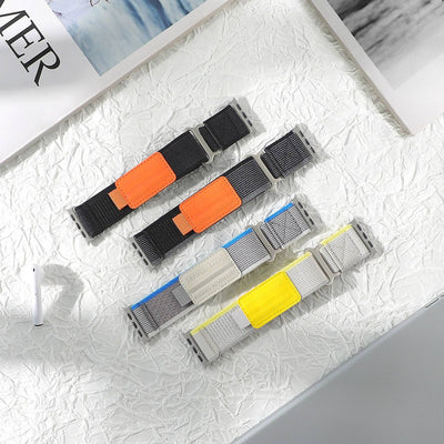 Collection of Adventure Straps for Apple Watch in various colors including black, gray, blue, and yellow, displayed on textured white surface.