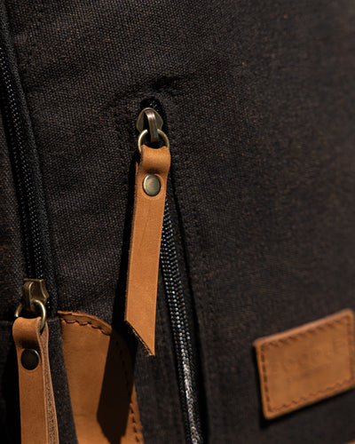 Close-up of a black backpack with brown leather straps and patches.