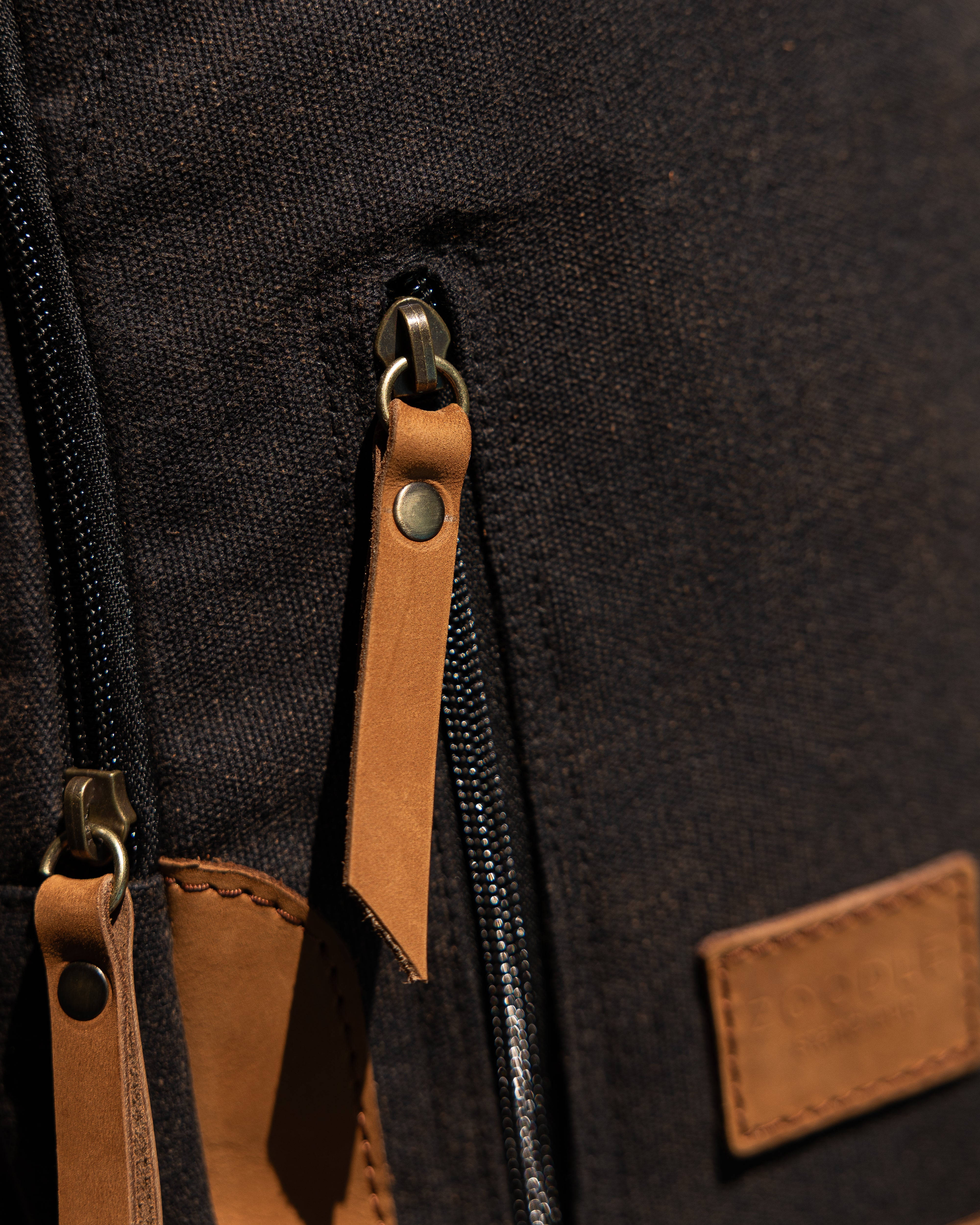 Close-up of a black backpack with brown leather straps and patches.